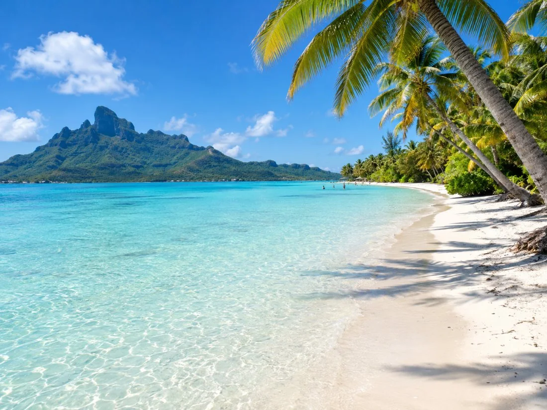 The long white sand of Matira Beach with palms and shallow turquoise water